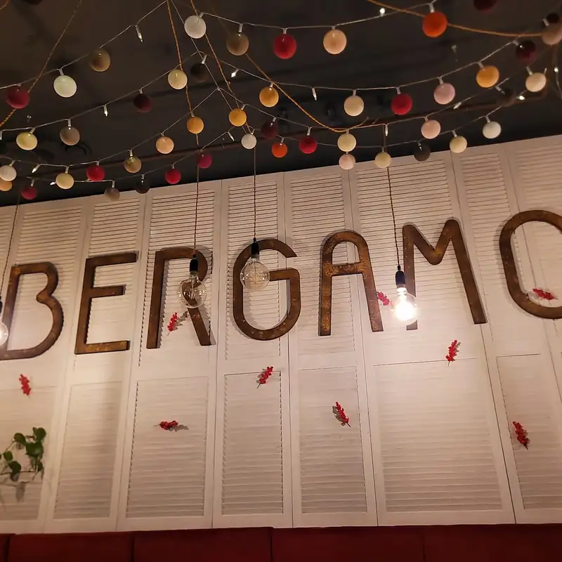 Napis BERGAMO na ścianie wyklejonej kartami menu, nad nim żarówki