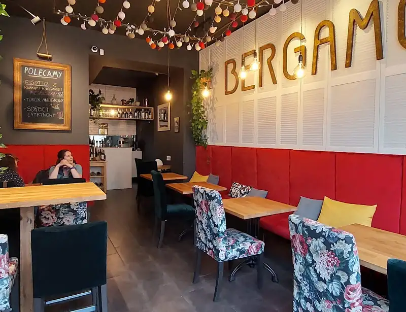 Sala z czerwonymi kanapami, drewnianymi stołami i girlandą żarówek