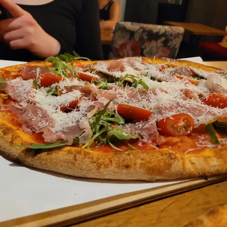Owalna pizza z prosciutto, rukolą i pomidorkami na papierze
