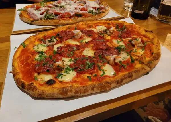 Owalna pizza z sosem pomidorowym, mozzarellą i salami na papierze